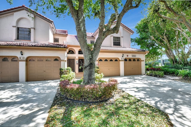 mediterranean / spanish-style home with a garage, driveway, stucco siding, and a tiled roof