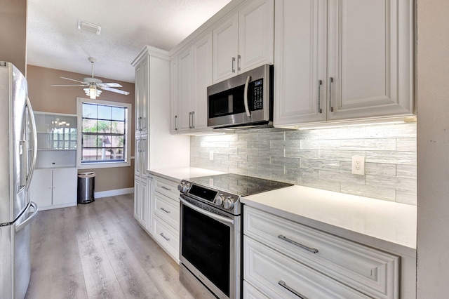 kitchen featuring light wood-style flooring, a ceiling fan, backsplash, white cabinetry, and stainless steel appliances