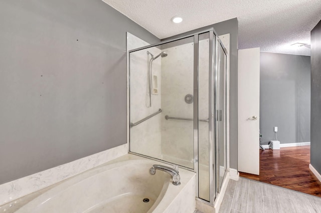 full bathroom with a garden tub, a textured ceiling, wood finished floors, a shower stall, and baseboards