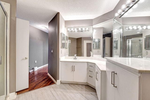 full bathroom featuring a stall shower, a textured ceiling, wood finished floors, baseboards, and vanity