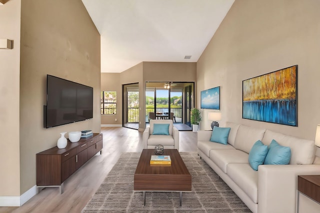 living room with baseboards, a ceiling fan, light wood-style floors, and a towering ceiling