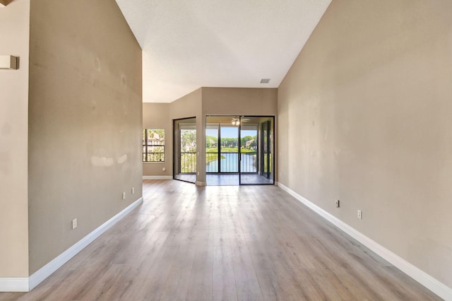 empty room with visible vents, a high ceiling, baseboards, and wood finished floors