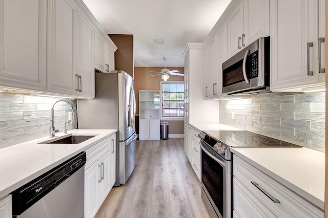 kitchen with appliances with stainless steel finishes, white cabinetry, light countertops, and a sink