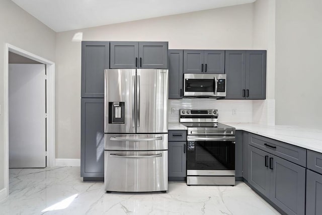 kitchen featuring light stone counters, lofted ceiling, gray cabinetry, stainless steel appliances, and marble finish floor