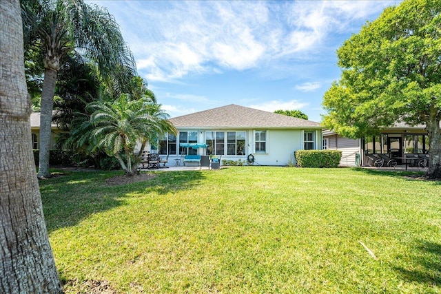 back of property with stucco siding, a shingled roof, a yard, and a sunroom