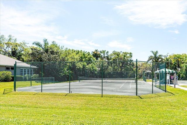 view of tennis court with a lawn and fence