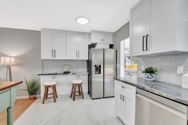 kitchen with decorative backsplash, dark stone countertops, appliances with stainless steel finishes, and marble finish floor