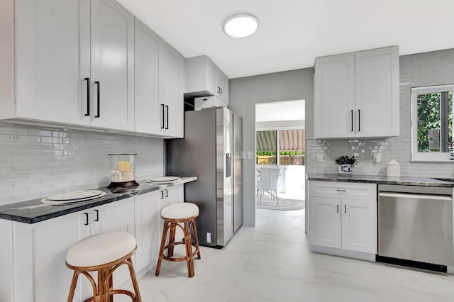 kitchen with dark stone countertops, appliances with stainless steel finishes, a kitchen breakfast bar, marble finish floor, and backsplash