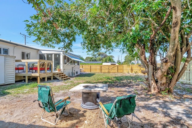 view of yard with a wooden deck, a fire pit, a fenced backyard, and a sunroom