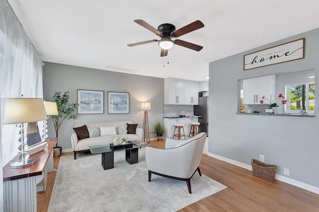 living area with light wood-type flooring, baseboards, and ceiling fan