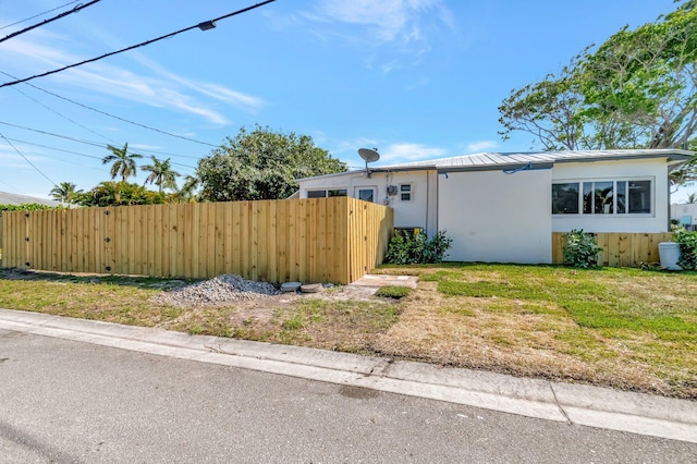 view of side of property with metal roof, fence, and stucco siding