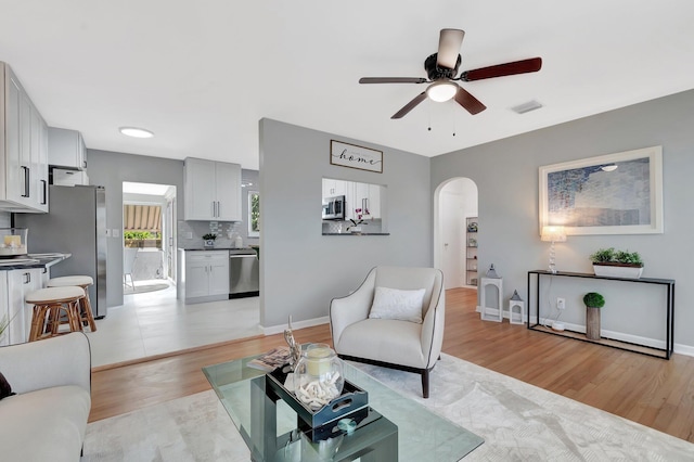 living area featuring visible vents, baseboards, arched walkways, ceiling fan, and light wood-style floors