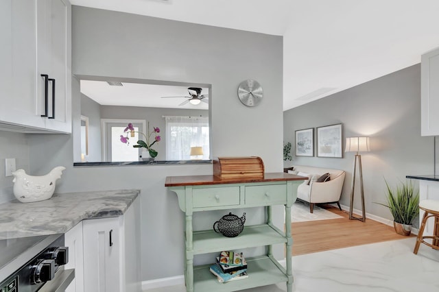 kitchen with baseboards, light stone countertops, light wood-style flooring, white cabinetry, and a ceiling fan