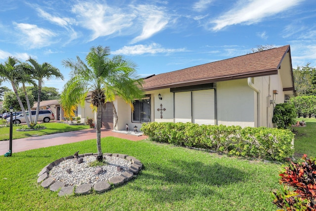 ranch-style house featuring stucco siding, driveway, a front lawn, roof with shingles, and a garage