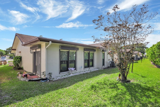 back of house featuring a yard, central AC unit, and stucco siding