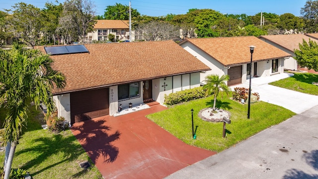 single story home featuring a front yard, an attached garage, stucco siding, concrete driveway, and roof mounted solar panels