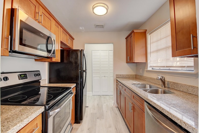 kitchen featuring brown cabinetry, light wood-type flooring, appliances with stainless steel finishes, and a sink