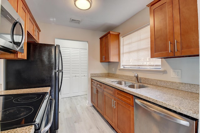 kitchen featuring light wood-style flooring, appliances with stainless steel finishes, brown cabinets, and a sink