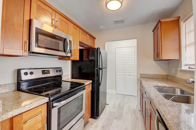 kitchen featuring visible vents, light wood-style flooring, appliances with stainless steel finishes, brown cabinets, and a sink