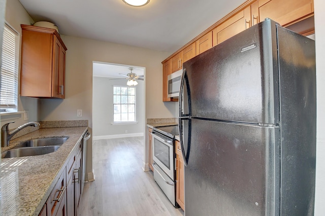 kitchen featuring light wood-style flooring, a sink, stainless steel appliances, baseboards, and light stone countertops