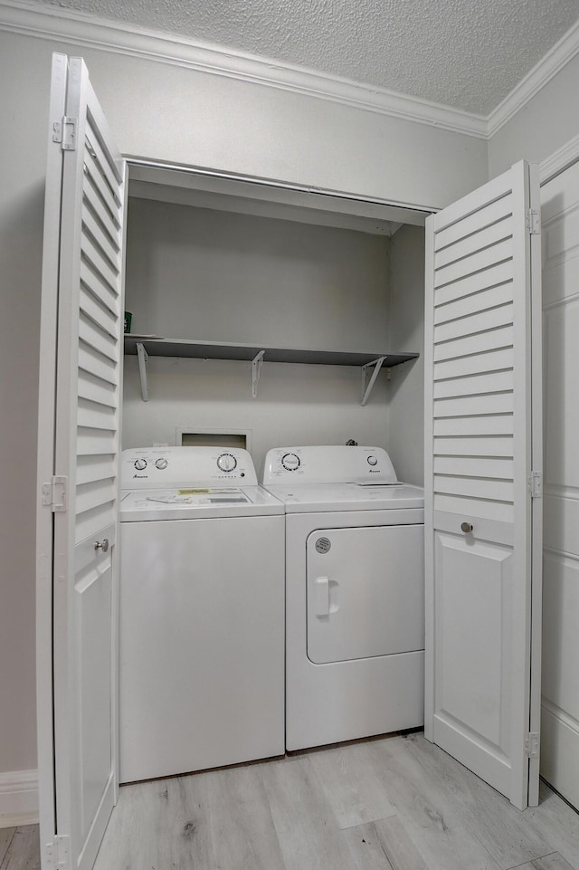 clothes washing area with washing machine and clothes dryer, laundry area, a textured ceiling, crown molding, and light wood-type flooring