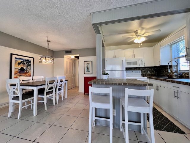 kitchen with white appliances, visible vents, a sink, white cabinets, and tasteful backsplash