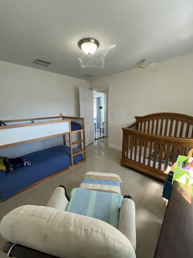 bedroom featuring tile patterned floors, visible vents, baseboards, and a textured ceiling