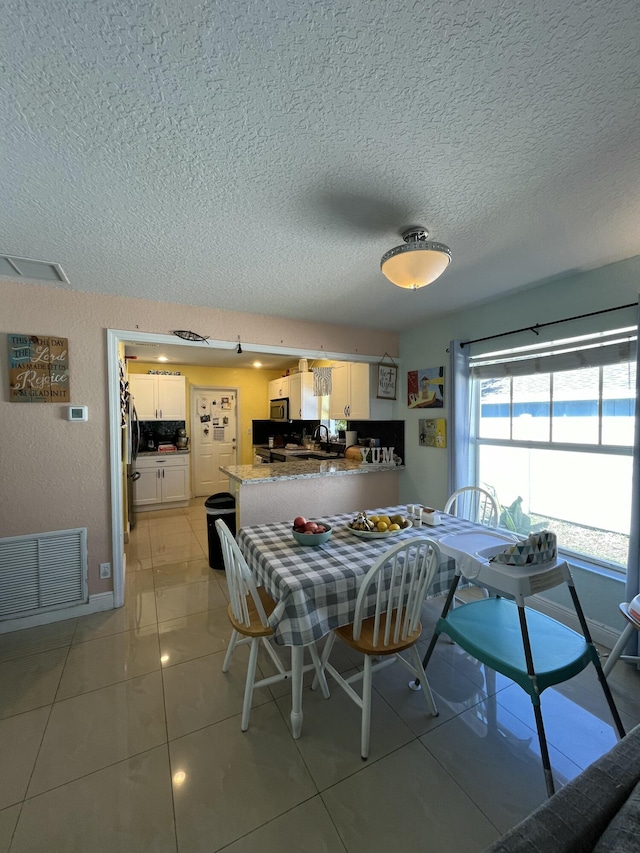 dining space featuring light tile patterned floors, visible vents, and a textured ceiling