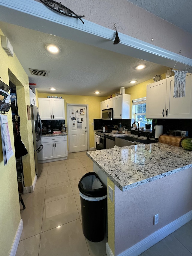 kitchen featuring visible vents, stainless steel microwave, range with electric stovetop, freestanding refrigerator, and white cabinetry