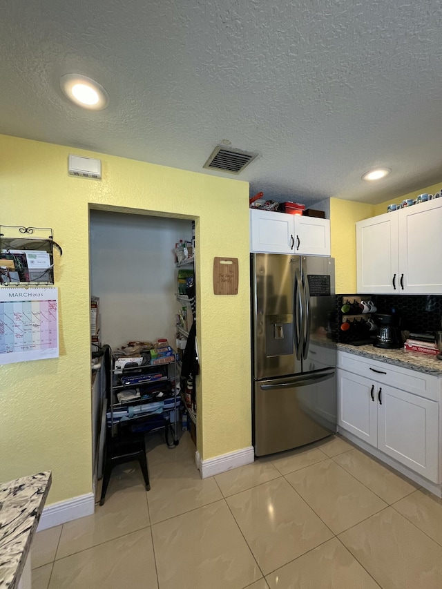 kitchen with light tile patterned floors, visible vents, stainless steel fridge, and white cabinetry