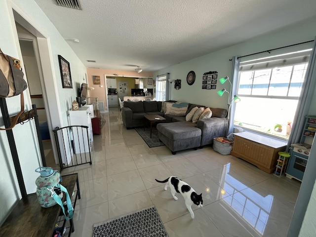 living area featuring light tile patterned floors, visible vents, and a textured ceiling