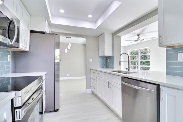 kitchen featuring a ceiling fan, a sink, a tray ceiling, appliances with stainless steel finishes, and light countertops