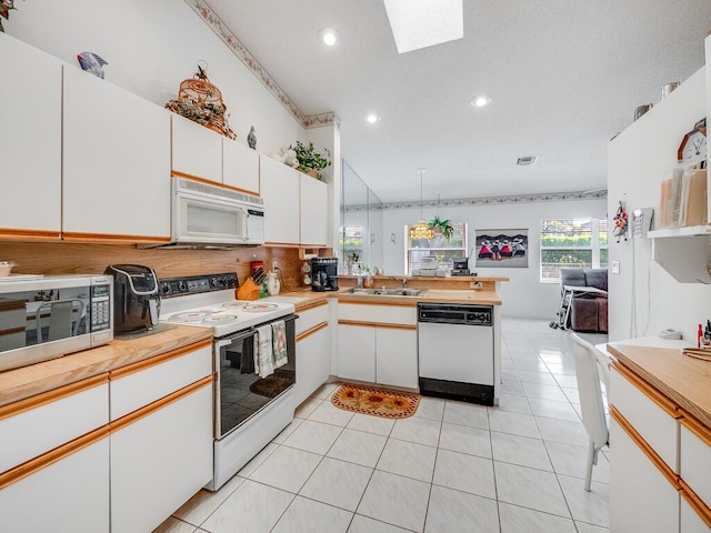 kitchen with light countertops, light tile patterned floors, white cabinets, white appliances, and a sink