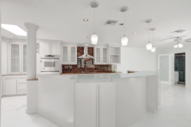 kitchen with white cabinetry, wall chimney range hood, visible vents, and marble finish floor