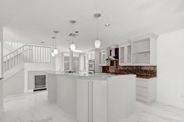 kitchen featuring oven, white cabinets, marble finish floor, wall chimney exhaust hood, and tasteful backsplash