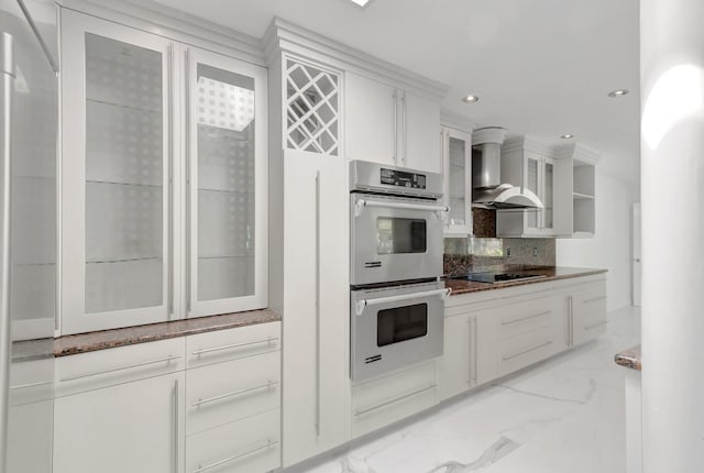 kitchen with marble finish floor, white cabinetry, double oven, wall chimney exhaust hood, and glass insert cabinets