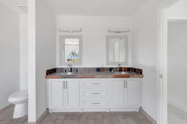 full bathroom with double vanity, toilet, baseboards, and a sink