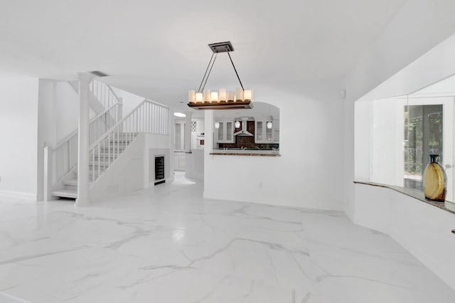 unfurnished living room with a chandelier, stairway, marble finish floor, and visible vents