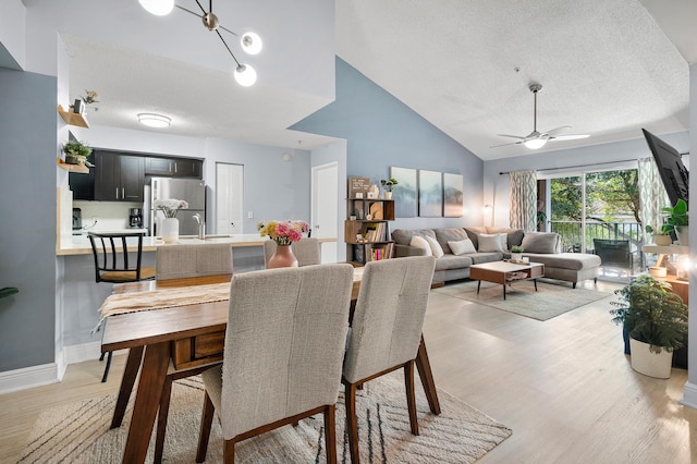 dining space with baseboards, lofted ceiling, light wood-style floors, a textured ceiling, and a ceiling fan