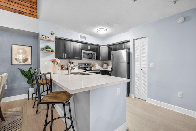 kitchen featuring a breakfast bar, a peninsula, a sink, stainless steel appliances, and light countertops