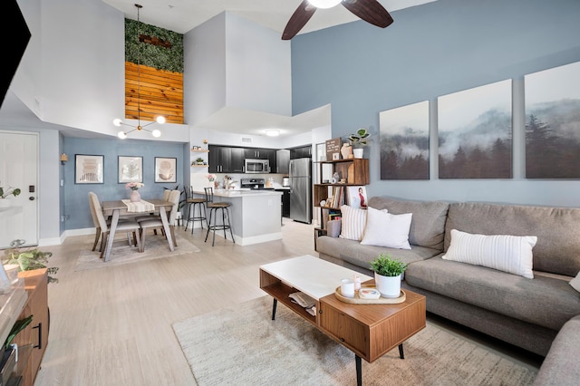 living room featuring a towering ceiling, baseboards, light wood-style flooring, and a ceiling fan