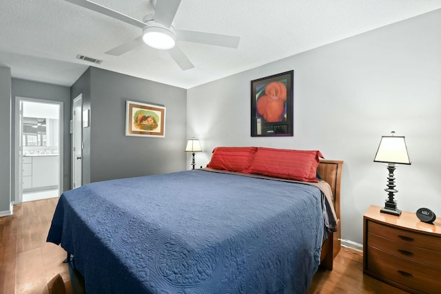 bedroom with wood finished floors, visible vents, ceiling fan, a textured ceiling, and connected bathroom