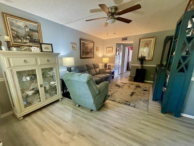 living area featuring a ceiling fan, visible vents, baseboards, a textured ceiling, and light wood-type flooring