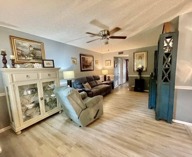 living room featuring a textured ceiling, visible vents, light wood-style flooring, ceiling fan, and a wood stove