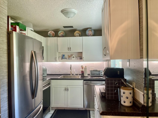 kitchen with visible vents, a sink, dark countertops, a textured ceiling, and appliances with stainless steel finishes