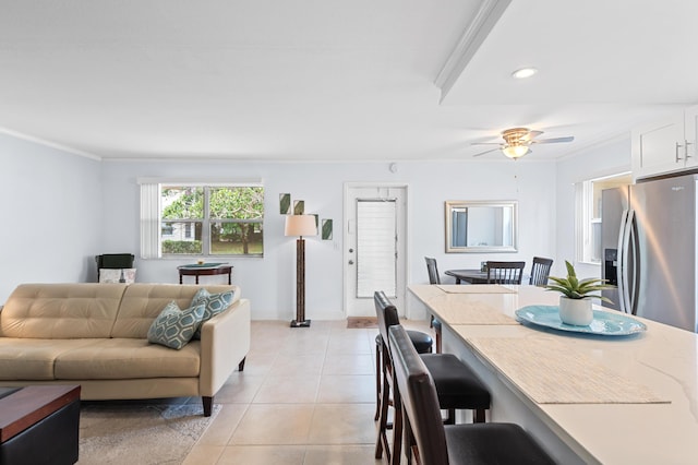 living area with light tile patterned flooring, a ceiling fan, baseboards, and ornamental molding