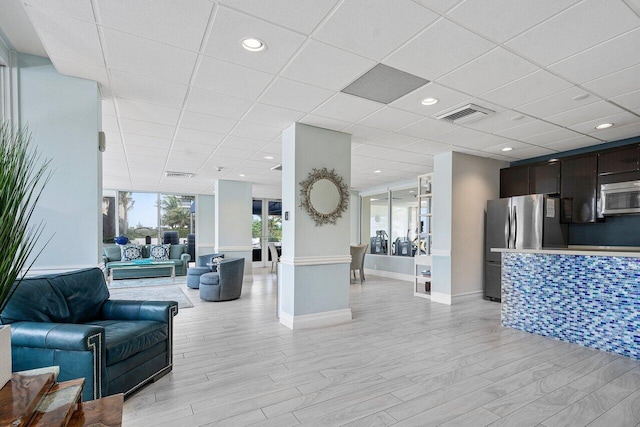 interior space with baseboards, visible vents, a drop ceiling, and light wood-type flooring