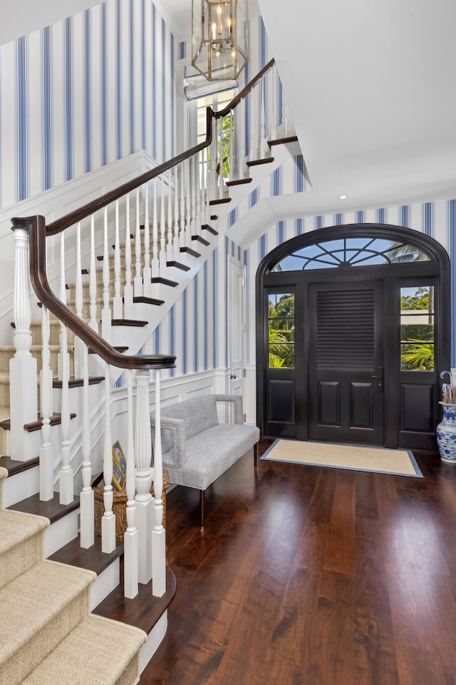 foyer featuring stairway, wood finished floors, wallpapered walls, an inviting chandelier, and wainscoting