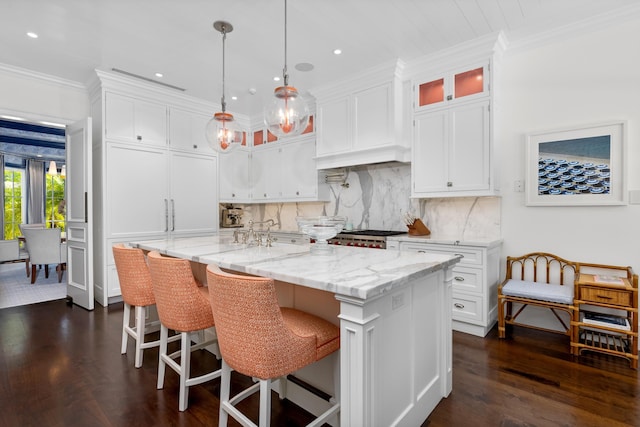 kitchen with a kitchen island with sink, decorative backsplash, white cabinets, and ornamental molding