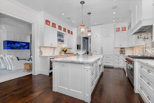 kitchen with light stone counters, an island with sink, stainless steel range, custom range hood, and white cabinetry